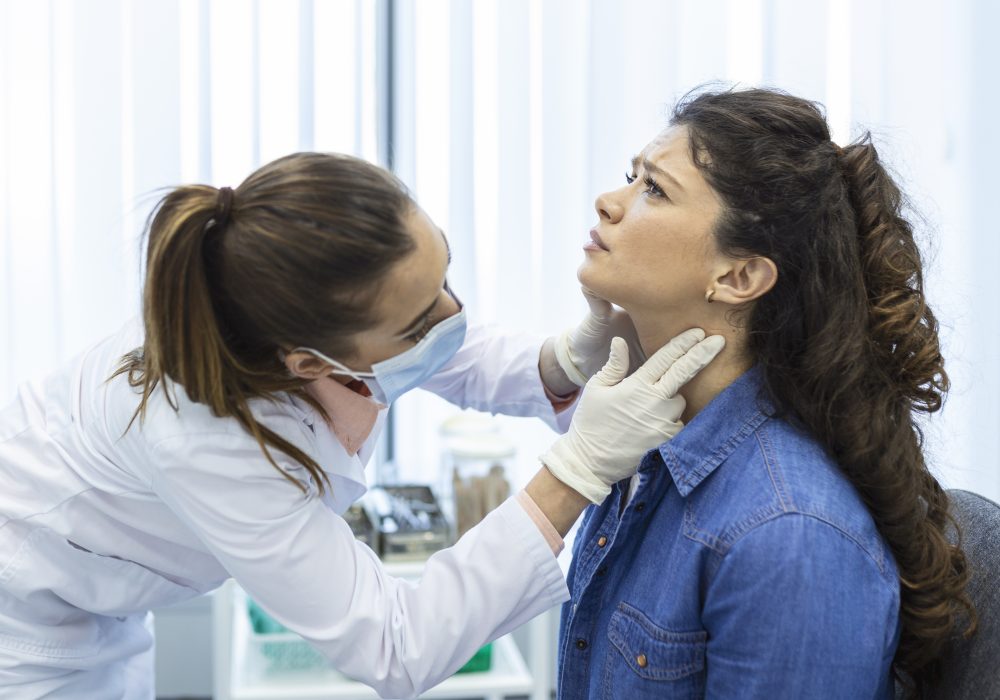 Endocrinologist examining throat of young woman in clinic. Women with thyroid gland test . Endocrinology, hormones and treatment. Inflammation of the sore throat